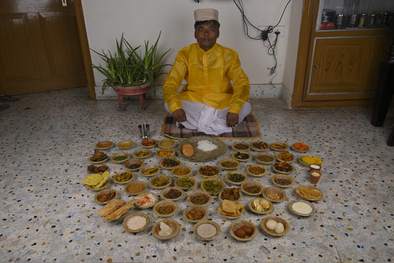 A man in traditional Maithili clothing sitting for the special 56 Bhog thali.